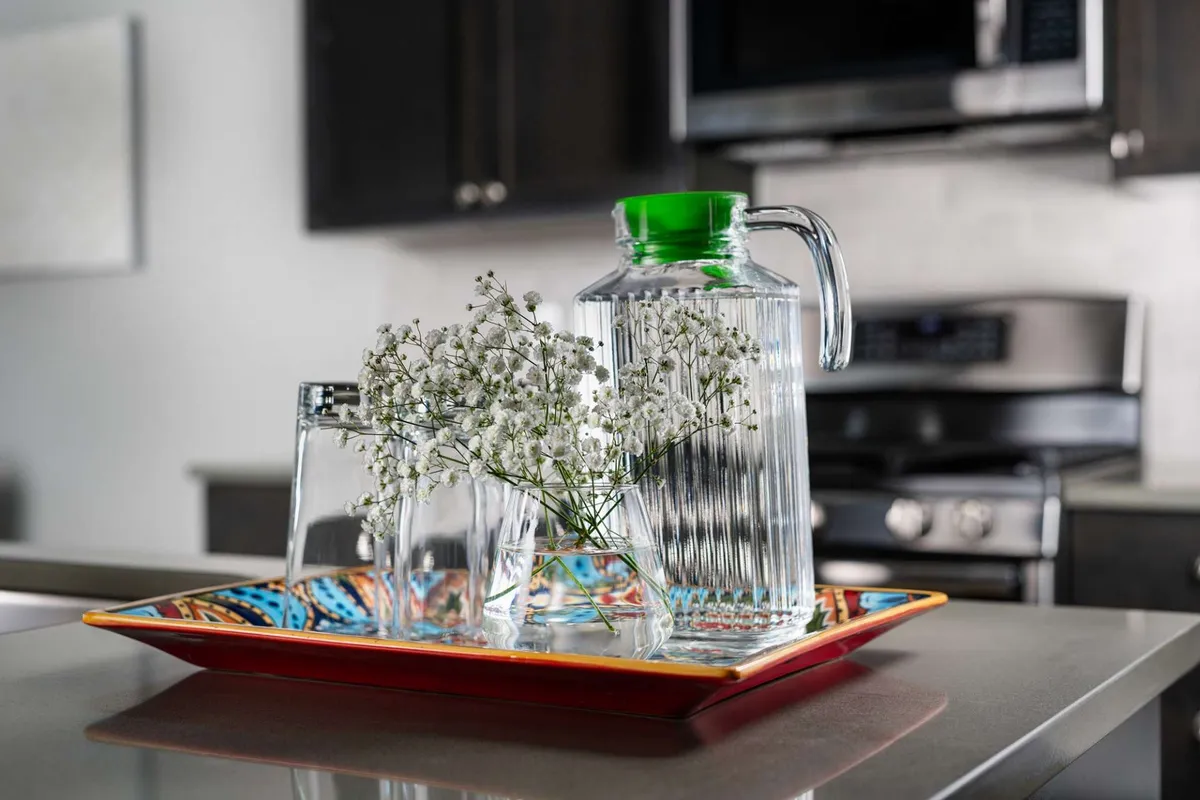 A warmly lit interior scene displaying a glass pitcher with green lid, three glasses, and a decorative floral tray, all set for guests. The inviting arrangement suggests moments of togetherness and hospitality, echoing themes of family gatherings and shared experiences.