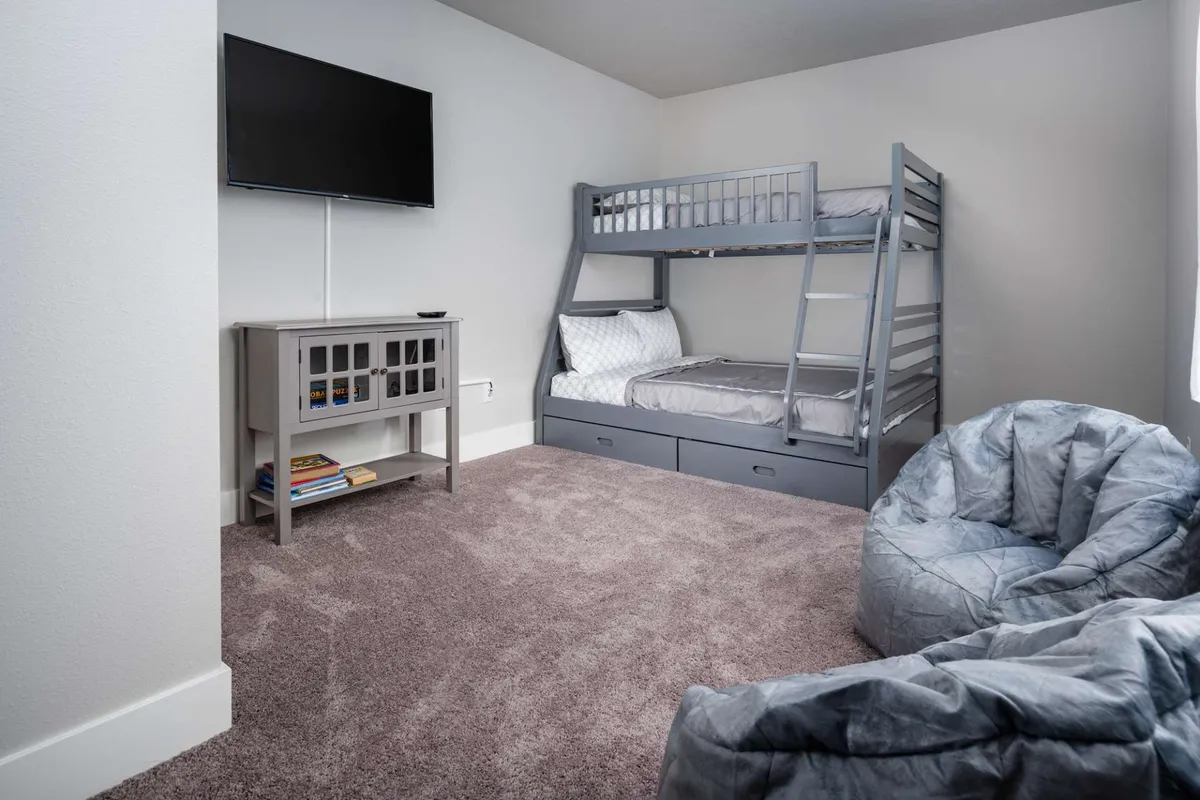 A playful and inviting kids' room with a bunk bed, bean bag chairs, a TV, and a small storage cabinet. The space is designed for both sleep and play, making it perfect for children or group sleepovers. The relaxed vibe encourages both fun and rest.