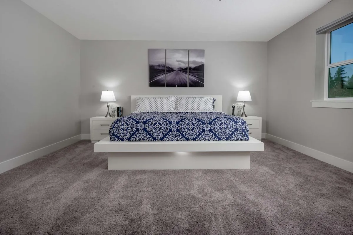 A serene bedroom featuring a bed with a stylish patterned duvet, modern nightstands and lamps, and a piece of artwork above the bed. The room is softly lit, creating a tranquil atmosphere ideal for rest and relaxation. Natural light gently filters in, enhancing the peaceful ambiance.