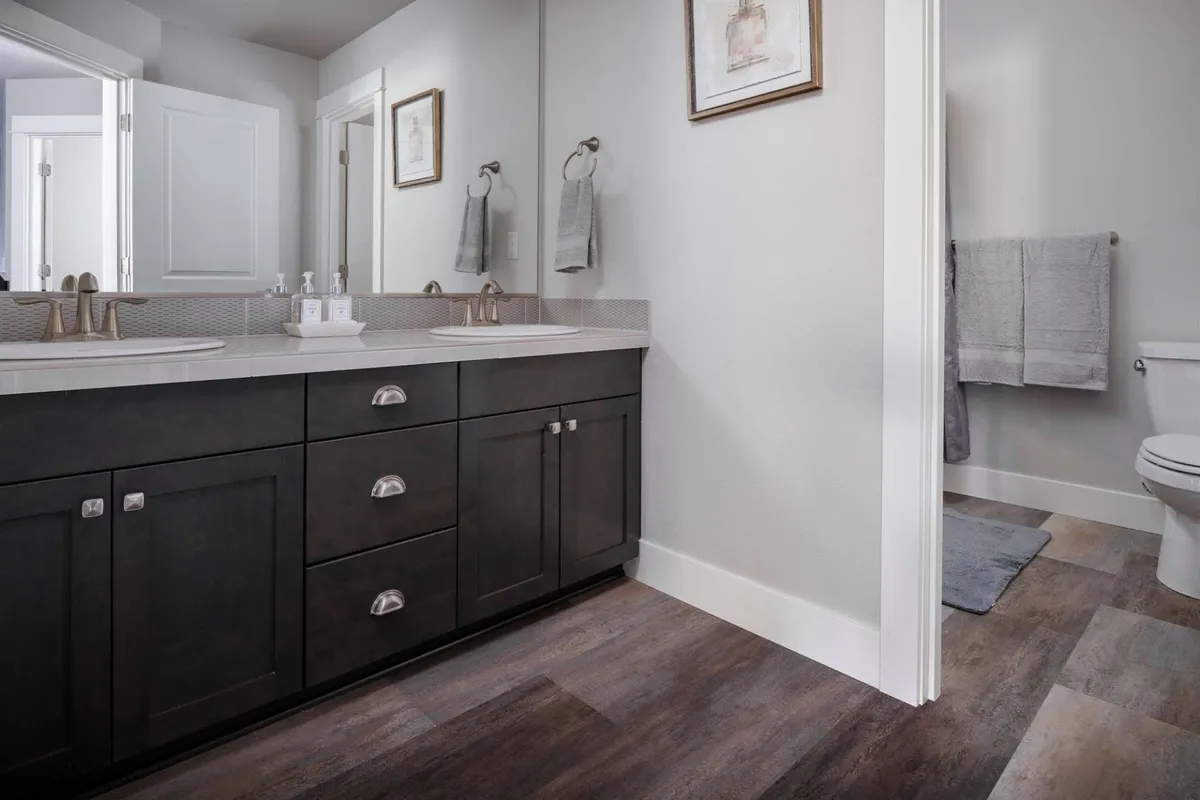 A modern double vanity bathroom with a mirrored wall, sleek faucets, and tasteful artwork. The clean, organized space is perfect for morning routines or unwinding in the evening, and can easily represent the accessible main-level bath.